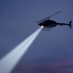 police helicopter shining a light beam in the dark sky